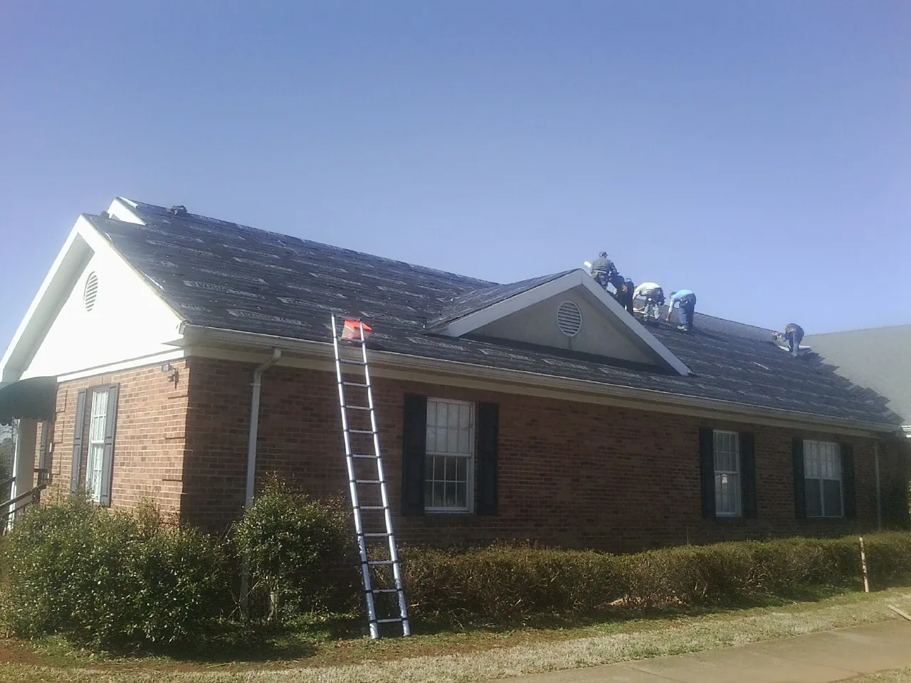 Crew tearing shingles off a brick ranch roof with a ladder set — Emergency Roof Repair work by our crew in Stennis Space Center