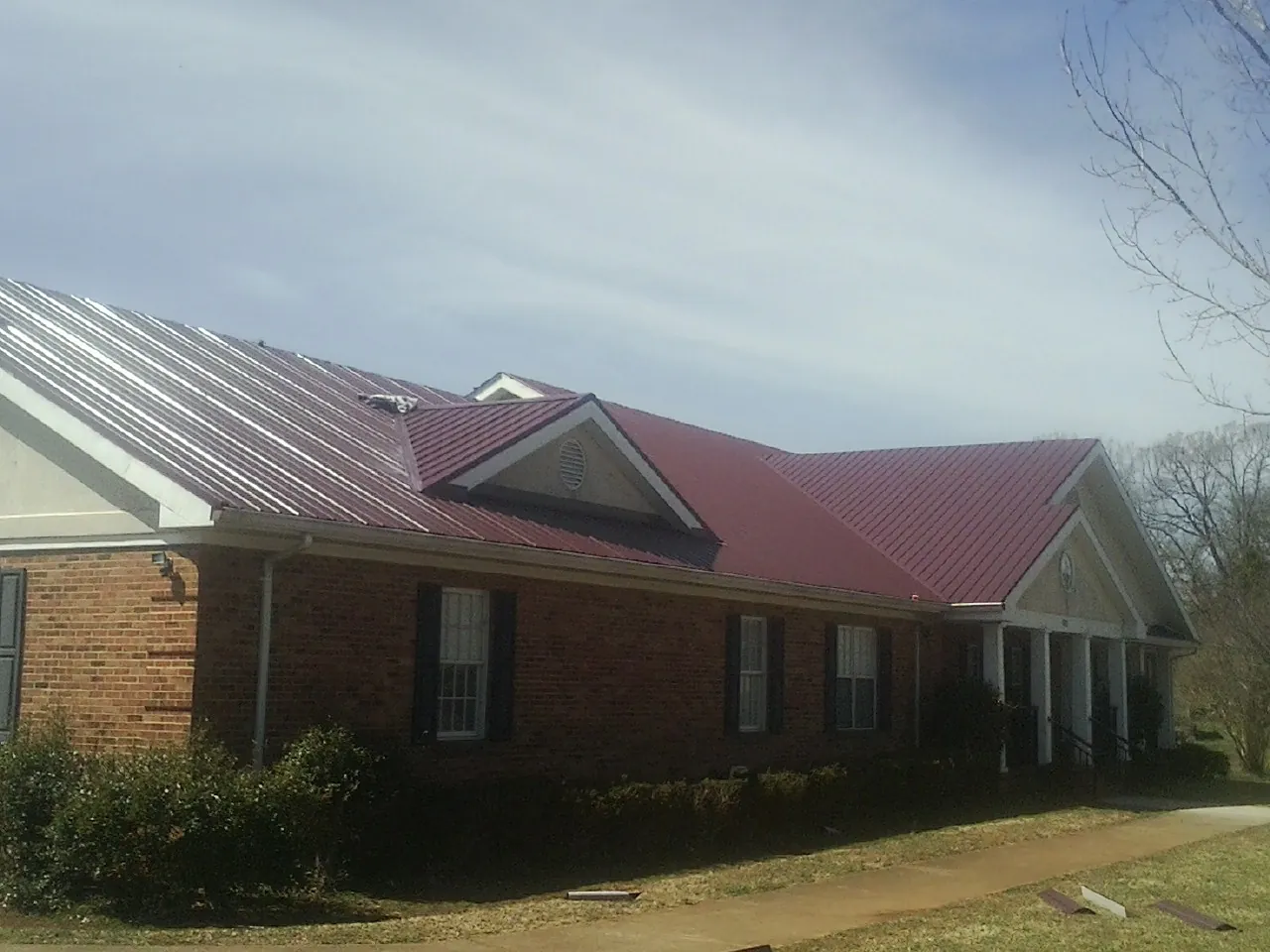 Red metal roof with gabled entries on a long brick building, from a Hail Damage Roof Repair job in Stennis Space Center
