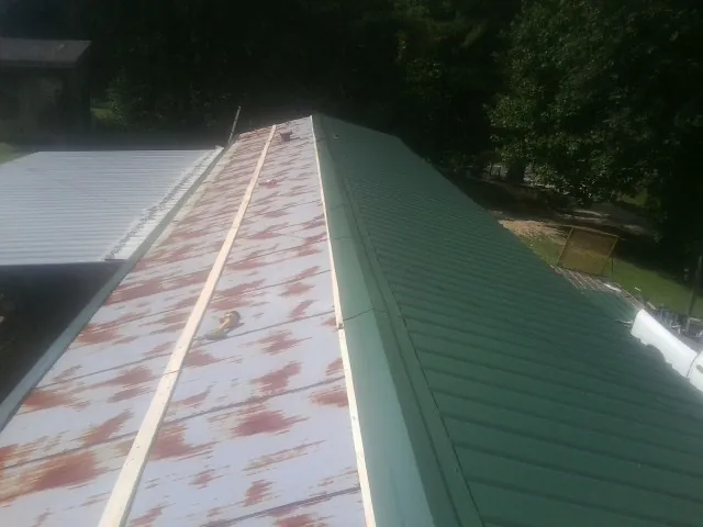 Old rusted panels beside newly installed green metal roofing — Wind Damage Roof Repair by Roofing Brothers in Stennis Space Center