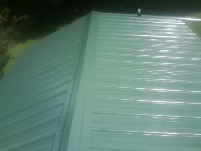 New green metal panels meeting at the ridge of a roof — Flat Roof Repair work by our crew in Stennis Space Center