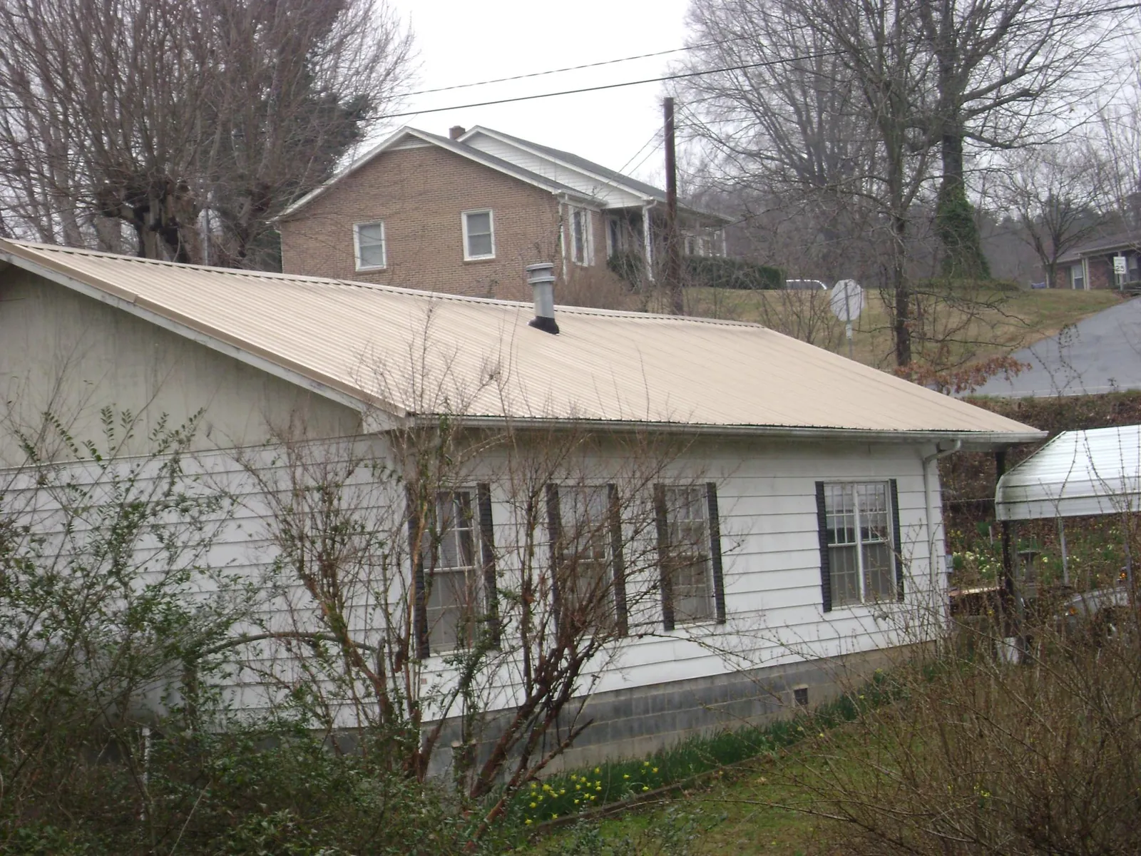 Tan metal roof on a white sided house set into a hillside — Commercial Roofing by Roofing Brothers in Stennis Space Center